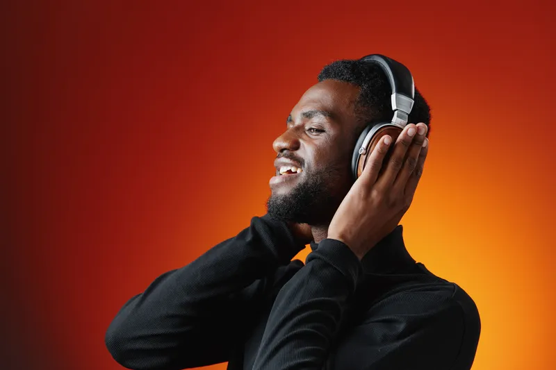 Happy Black man enjoying music through headphones with a vibrant orange background, showcasing a joyful expression and modern style