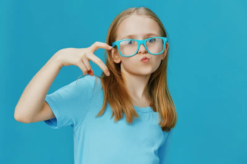 Young girl with glasses making a peace sign on a vibrant blue background, showcasing casual style and a playful mood Ideal for themes of youth and creativity