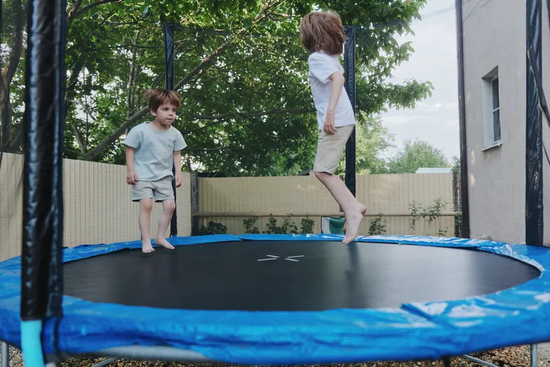 Jumping kids on a trampoline enjoying the summer sun with laughter and excitement in a backyard filled with greenery and natural light.