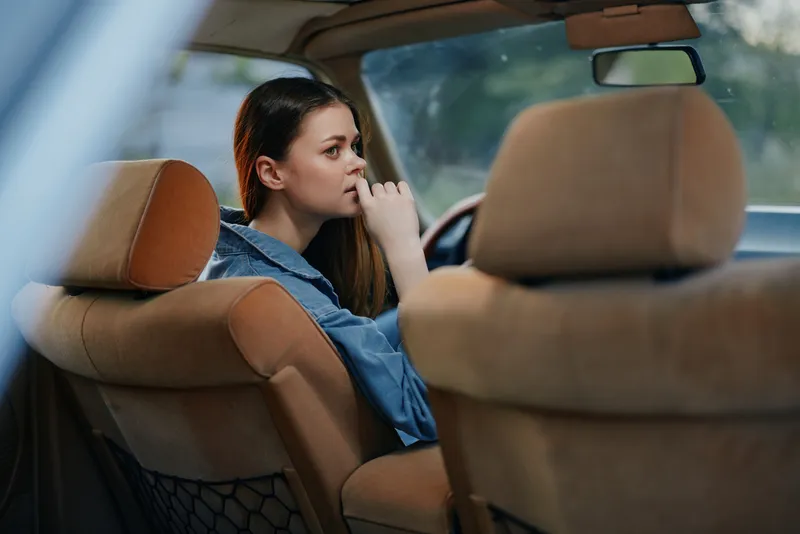 Thoughtful young woman sitting in a car, lost in deep contemplation, reflecting on life decisions with a serious expression.