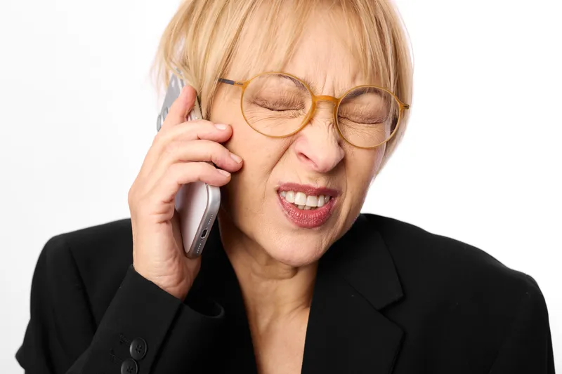 Woman senior business phone stress, call, glasses, frustrated expression, holding smartphone to ear, close up on background, communication at work, headache