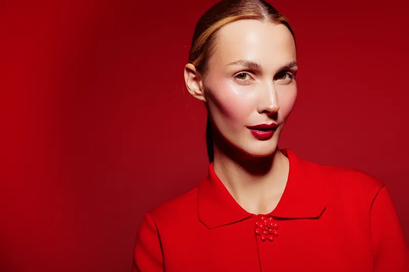 Portrait of confident woman with red lipstick and red sweater on red background. Studio lighting highlights her clear skin and elegant expression. Concept of beauty and fashion.