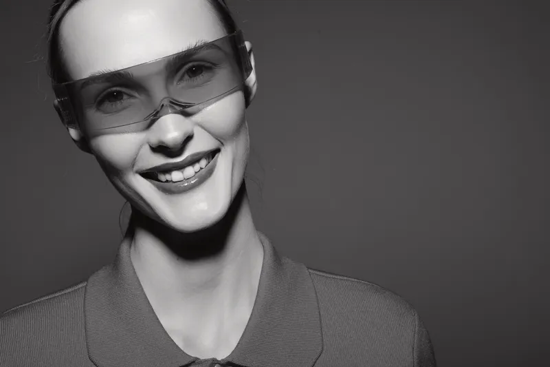 Smiling young white woman with pale skin wearing transparent fashion glasses and a polo shirt poses against a dark background in a studio. Concept for style, fashion, and portrait.