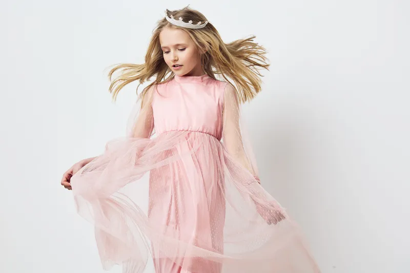 Elegant young girl in a flowing pink dress, showcasing grace and joy against a soft white background Ideal for fashion and childhood concepts