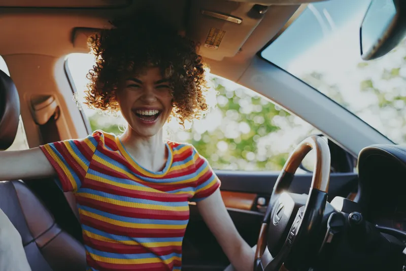 Woman enjoys a joyful car ride, lifestyle shot with striped shirt, retro film color vibe, bright sunlight inside the cabin, candid and cheerful, capturing a casual, happy moment.