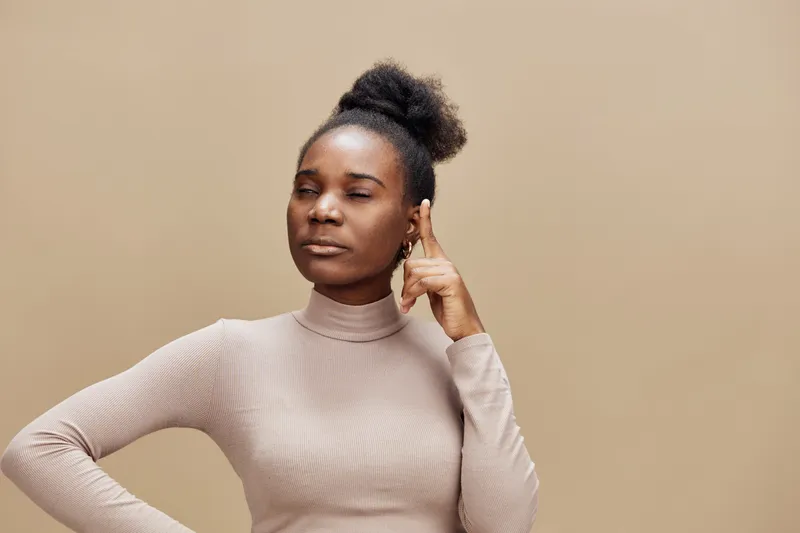 Thoughtful young woman in a beige top reflecting on ideas, with a contemplative expression and a minimalist warm background for lifestyle concepts