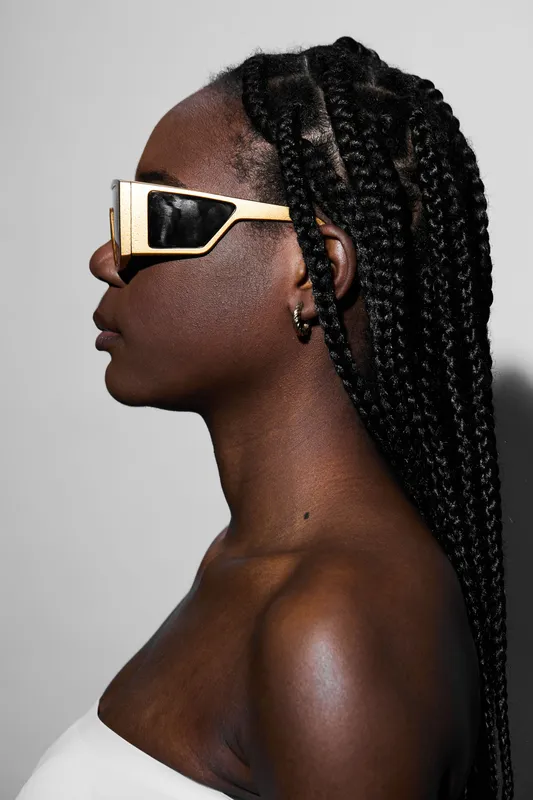 Fashionable black model with braided hair wearing stylish sunglasses against a minimalist background showcasing confidence and modern trends