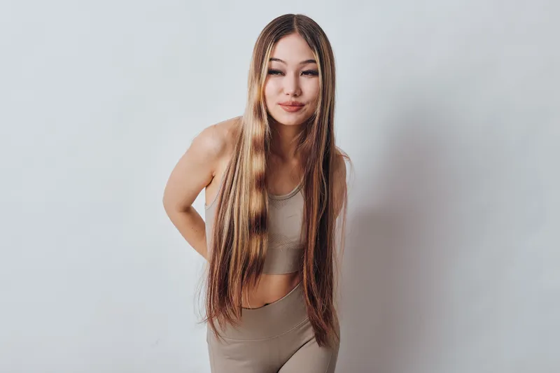 Young woman with long braided hair posing in sportswear against white background for fitness, fashion, beauty, and lifestyle concept in studio.