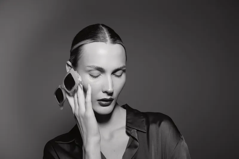 Young caucasian woman with pale skin and dark hair holds ice pack on face with closed eyes in black shirt. Concept of pain relief and self care.