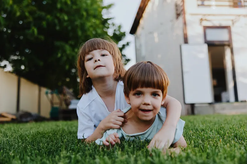 Two playful children enjoying a sunny day, laughing and exploring the lush green grass, embodying the joy of childhood innocence and friendship.