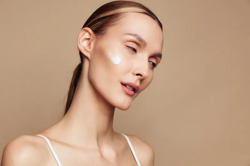 Woman applying face cream, close up portrait, smooth skin, skincare self care and beauty concept, beige background, soft studio lighting, calm expression, wellness