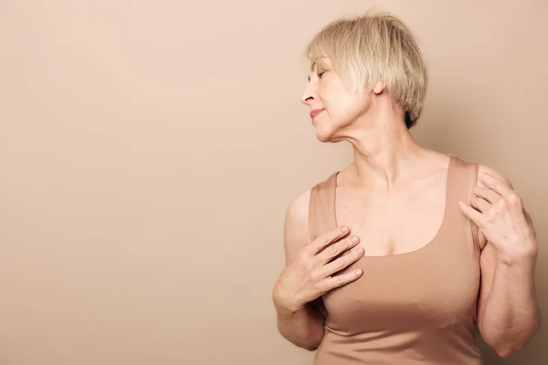 Portrait of mature woman with short blonde hair in beige top posing sideways against neutral background. Concept of aging, confidence, beauty, lifestyle, and natural skin care.