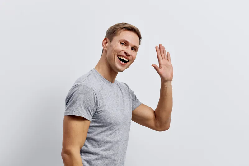 Smiling happy young caucasian man wave hand greeting casual gray t-shirt isolated on white background friendly gesture digital nomad concept