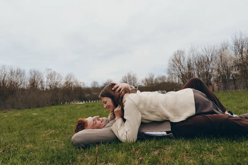 Young couple lying on green grass in a park during autumn while smiling and enjoying a tender moment together in casual warm clothing.