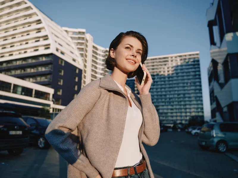 A cheerful professional woman is seen texting on a mobile phone in a modern urban street. She smiles, appears confident and engaged, creating a positive and dynamic city atmosphere.