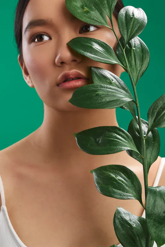 asian woman portrait with leafy plant partially obscuring her face against a vibrant green backdrop, serene expression, natural beauty and botanical mood