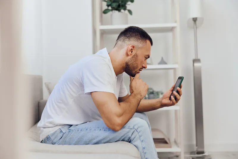 Pensive man engrossed in smartphone, showcasing modern lifestyle and digital connection with a touch of minimalism and tranquility, ideal for contemporary themes.