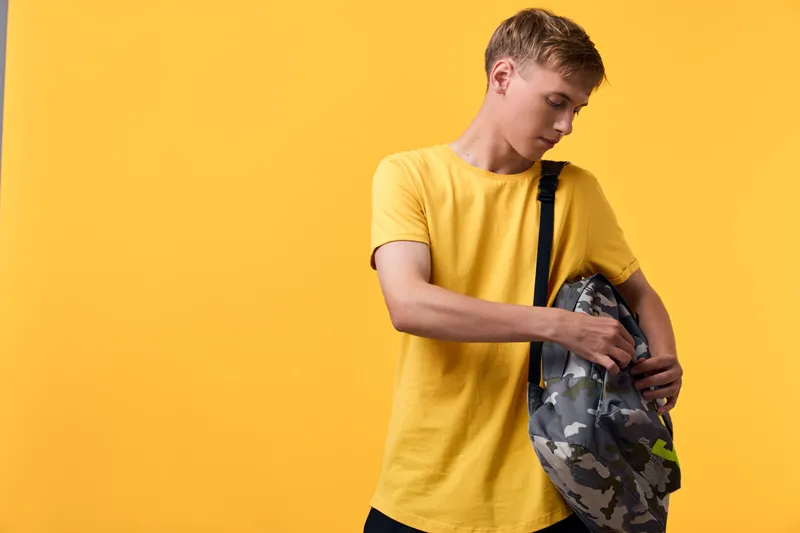 Youth wearing a yellow tee with a camouflage backpack on a bright backdrop, presenting casual style, travel readiness, movement and everyday adventure.