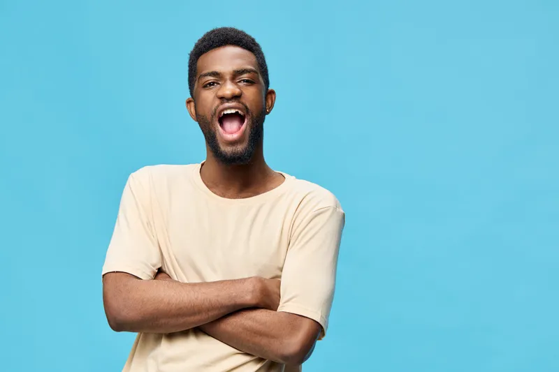 A joyful young African man smiling against a bright blue background, showcasing excitement and confidence in casual light clothing