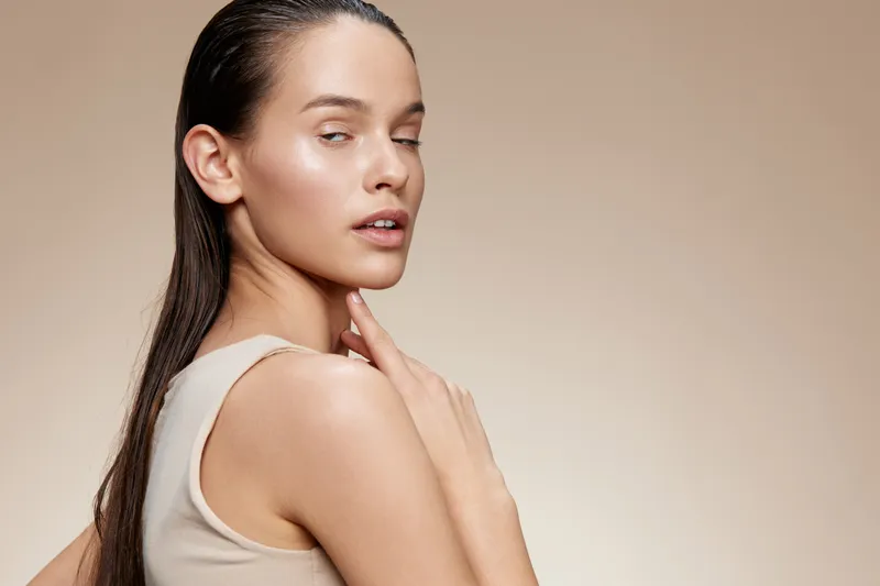 Elegant woman with long hair wearing a beige top, showcasing a natural beauty look with a soft, neutral background, evoking feelings of calm and confidence