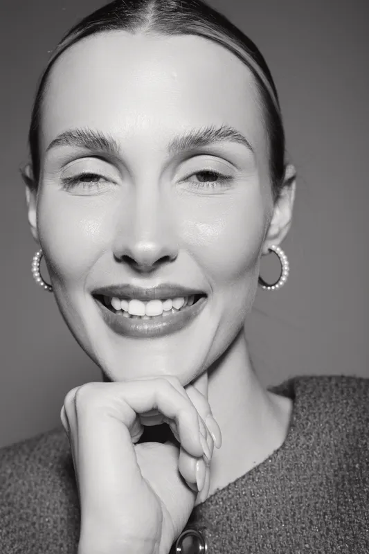 Close-up portrait of a smiling light skinned Caucasian woman with slicked back hair wearing hoop earrings and a textured top. Concept of happiness, beauty, and confidence.