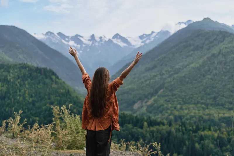 Woman in mountains raising arms for freedom and nature, authenticity inclusivity
