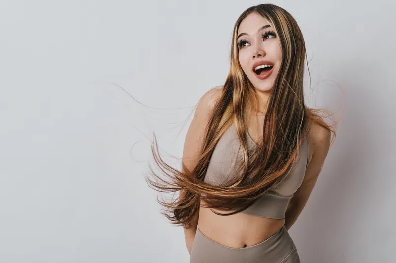 Young woman with long hair and casual outfit posing and smiling with excitement on light background for lifestyle and happiness concept.