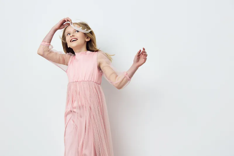 Happy girl in a pink dress dancing joyfully on a light background, embodying innocence and childhood wonder