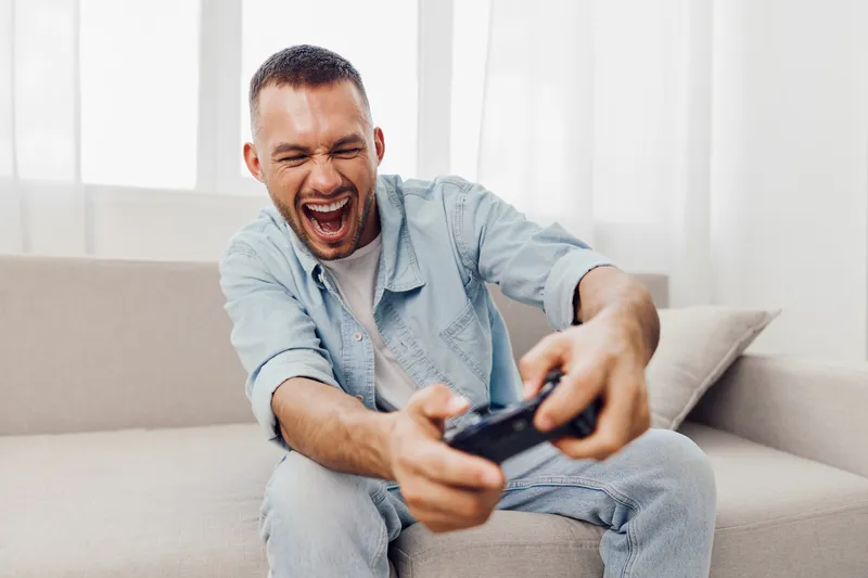 Excited man playing video games at home, expressing joy and engagement while enjoying a digital escape from daily life and technology. Concept: emotional release.