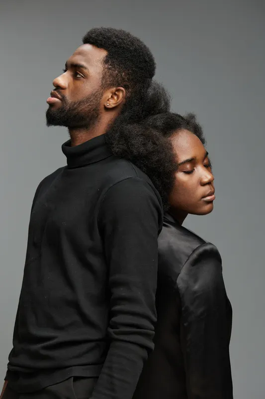 A stylish portrait of a Black couple in black attire, conveying deep emotions and connection in a minimalist gray background with soft lighting