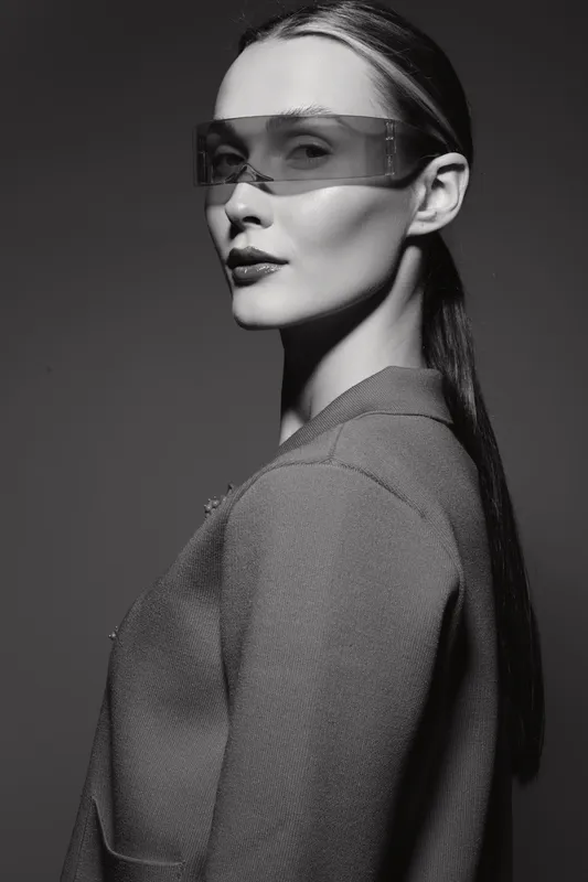 Portrait of a fair skinned Caucasian woman with slicked back hair wearing transparent visor and textured jacket in studio.
