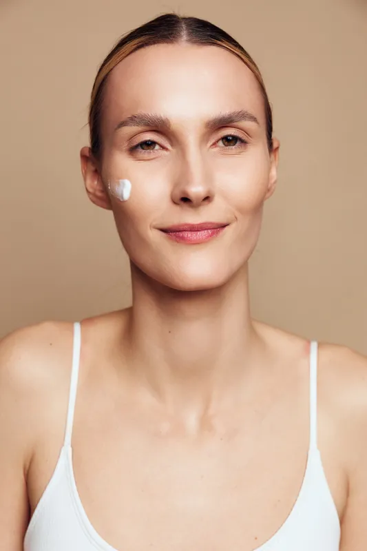 Woman close up with skincare treatment, white cream on cheek. Calm face, beauty and self care concept, wellness and cosmetic routine in minimal studio lighting for healthy skin today.