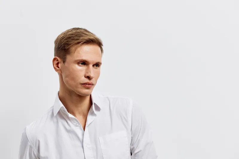 thoughtful young caucasian man in white shirt digital nomad work concept casual hairstyle looking aside isolated light background