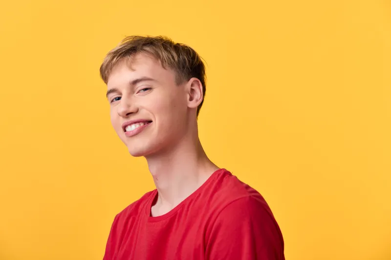 Smiling man in red shirt stands against a vibrant yellow background, conveying friendly confidence, casual style, and approachable mood suitable for lifestyle, fashion, or advertising stock