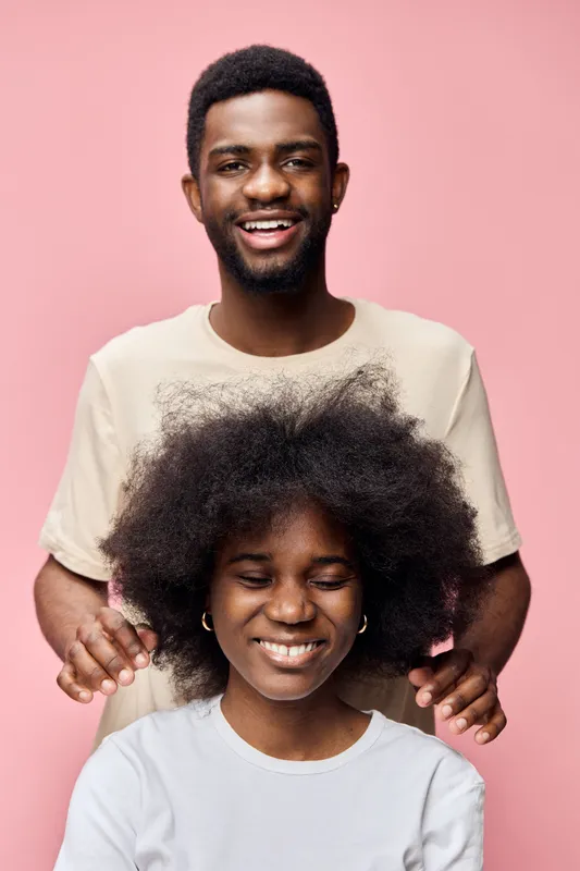 Cheerful young couple with natural hairstyles smiling against a pink background, representing love and joy in a vibrant and warm atmosphere