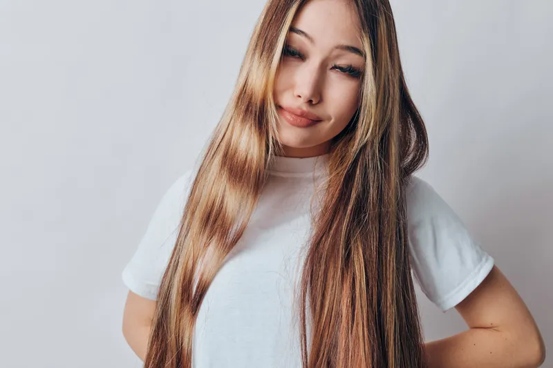 Woman with long straight hair wearing white t shirt posing against light background. Young female portrait with natural makeup and casual style in studio for beauty concept.