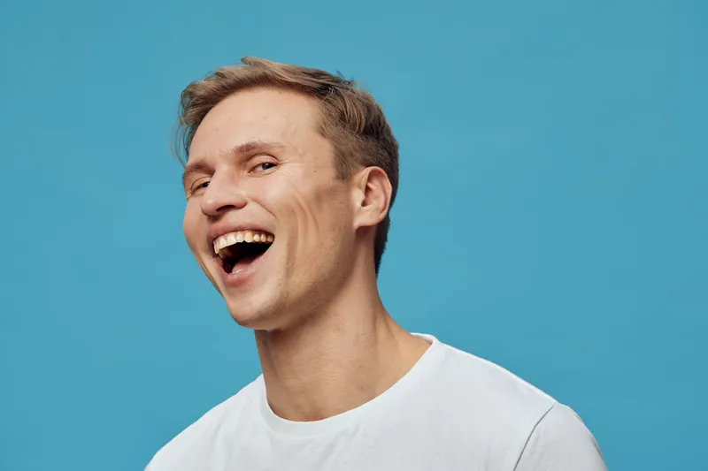 Smiling man with joyful expression wearing casual white t-shirt on blue background portrait. Happy, cheerful, positive emotion, studio shot, human face, emotion, lifestyle image, beauty, youth.
