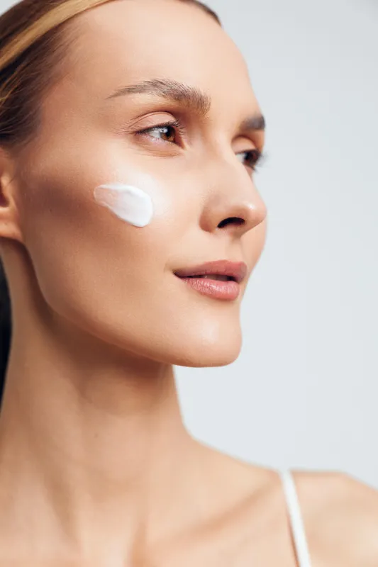 Skincare,beauty,woman,face,closeup,treatment,cosmetic,cream,moisturizer,dermatology,serene profile,white cream on cheek,soft studio light,smooth skin,minimal background