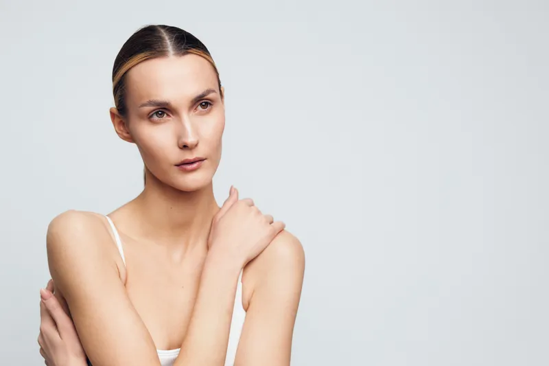 Woman skincare face moisturizer self care portrait studio lighting wellness close up clean background gently touches neck suggesting moisturizing skincare routine