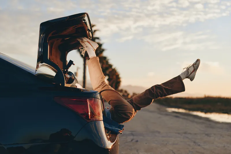 Woman lifestyle, car on road, sunset sunrise sky, travel mood, outdoors vehicle journey, casual denim boots and relaxed legs, golden light, seashore coastline beach horizon waves clouds