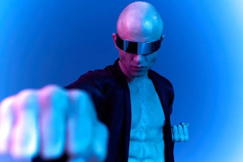 Strong man posing dramatically with a fist clenched, wearing futuristic sunglasses, showcasing a powerful presence in a vibrant blue light setting.