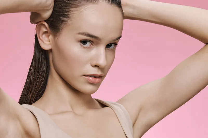 Young woman with long hair showcasing natural beauty against a pink background, evoking confidence and elegance in a minimalist style