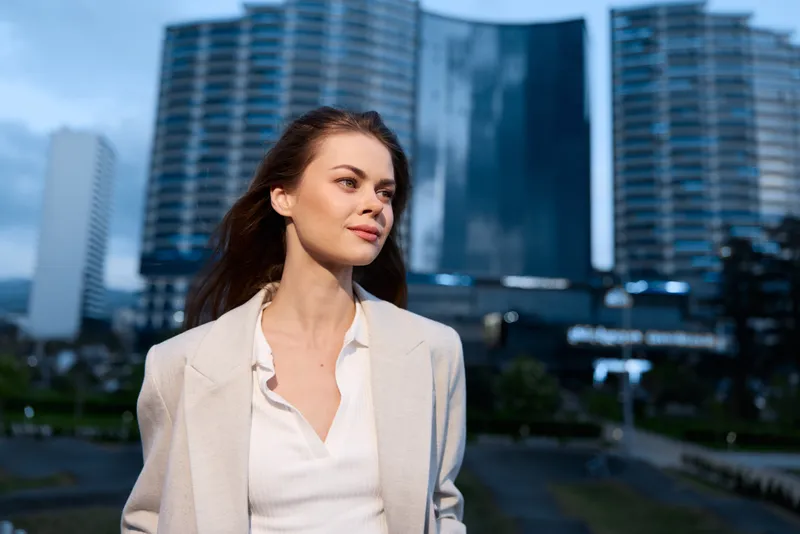 confident woman in beige blazer with city buildings background smiling outdoors modern lifestyle business concept