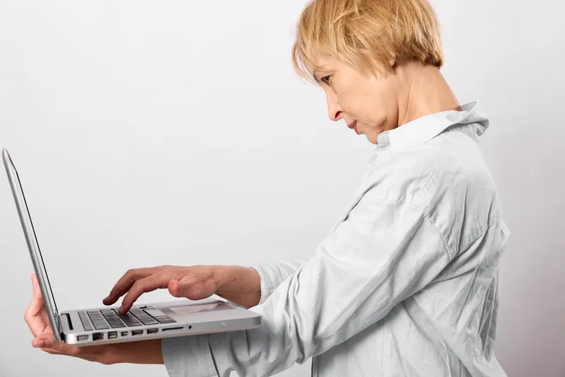 Woman using laptop, typing at keyboard, side view, technology and work concept, remote communication, white studio background, soft light, focused mood