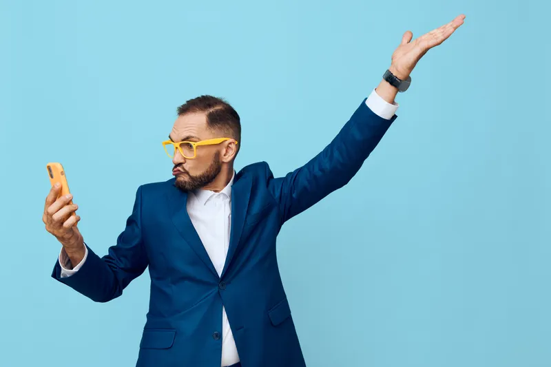 Professional business man stands against a vivid blue backdrop, isolated colorful background, projecting confident focus and curiosity while checking his mobile device.