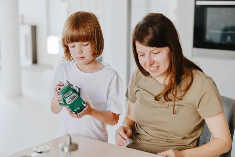 Caring woman engaging with a child while playing with a toy car, showcasing a warm family atmosphere and joyful moments together in a modern setting.