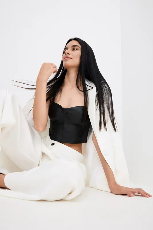 young woman sitting on the floor wearing stylish black top and white pants with a white jacket draped over her shoulders, relaxed pose and smooth long hair