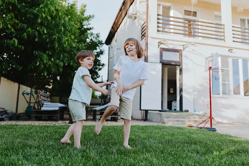 Two cheerful boys playing together in a sunny backyard, enjoying their time outdoors on a warm day, showcasing laughter and friendship in a joyful setting.