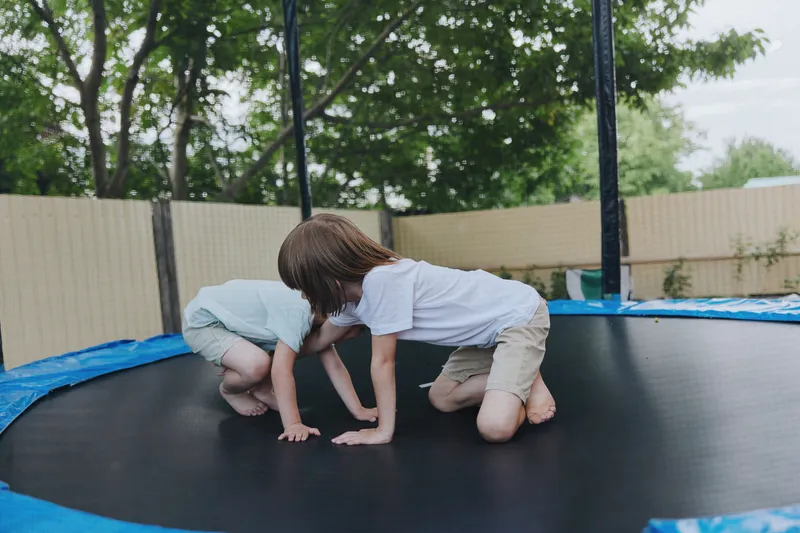 Curious boys playing on a trampoline in a green backyard, enjoying their time outdoors while displaying excitement and energy.
