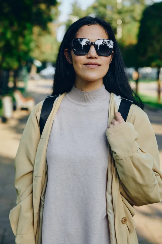 Woman wearing sunglasses, beige coat and turtleneck in a park setting, outdoor style, casual yet chic, showcasing street fashion and relaxed confidence under sunny daylight